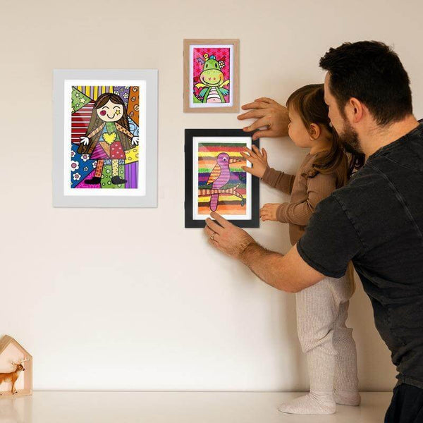 Father and child displaying colorful kids' art in modern frames on a wall, showcasing creativity and family bonding.
