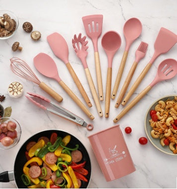 Silicone kitchenware utensils set in pink with wooden handles, ideal for cooking and baking, arranged with colorful vegetables.