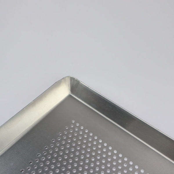 Close-up of a silver aluminum rectangular bakeware tray with perforated bottom and angled edges.