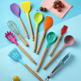 Colorful silicone kitchen utensils set with wooden handles on a blue background, featuring spatulas, whisks, and tongs.