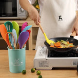 Colorful silicone kitchen utensils being used to stir vegetables in a frying pan on a stove.