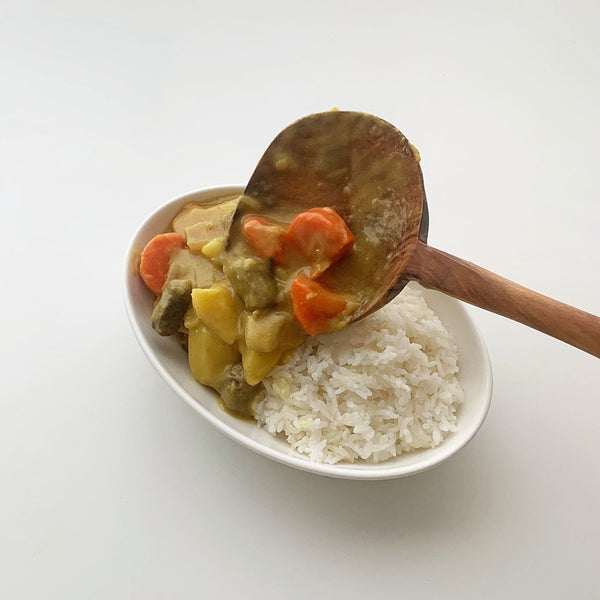 Wooden ladle serving curry with vegetables over a bowl of rice, showcasing modern Korean kitchen utensils.