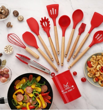 Red silicone kitchenware set with wooden handles, including spatulas, spoons, and tongs on a marble surface.